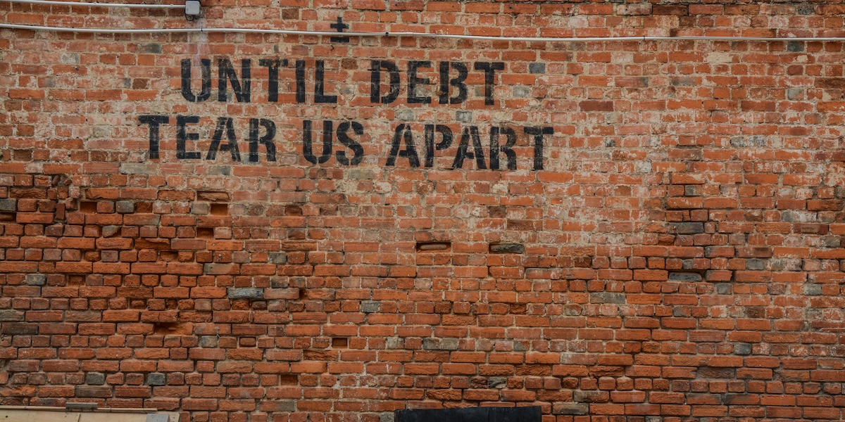 Brick wall with graffiti reading "till debt tear us apart" illustrating organizational change debt concept